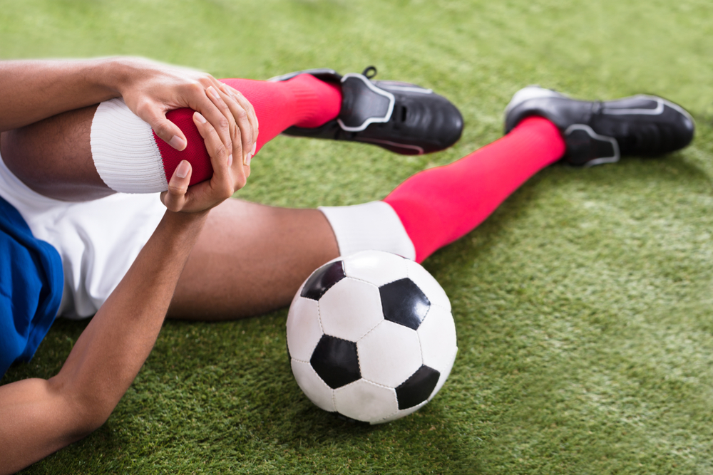 Voetballer met zwakke heupmusculatuur ligt op de grond met een knie blessure.