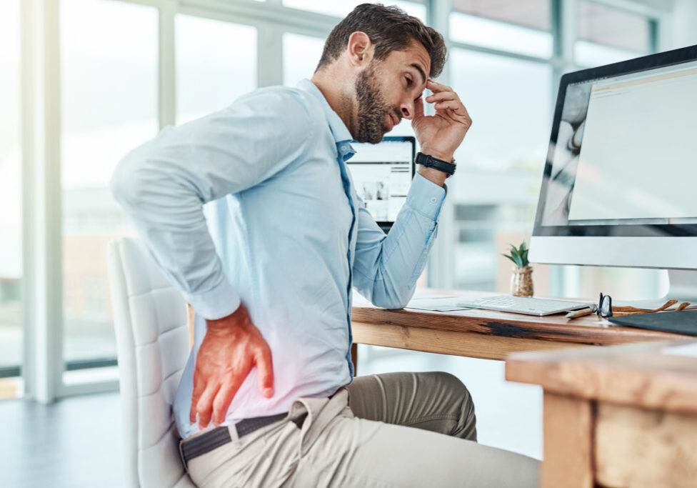 Shot of a young businessman suffering with back pain while working in an office