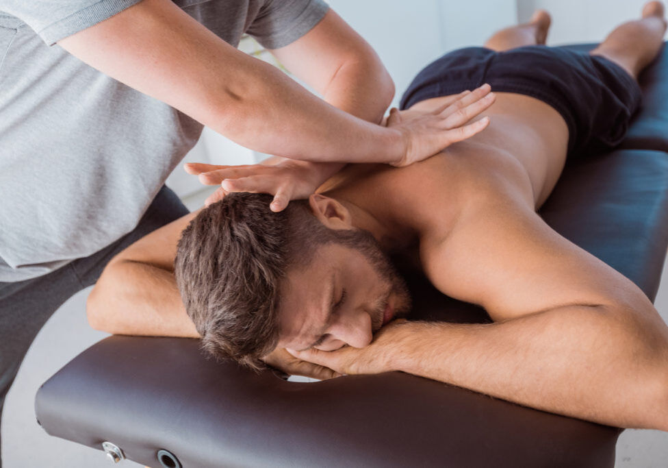 Close-up of a physical therapist giving back massage to a man lying on bed at rehab center
