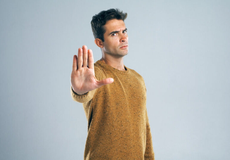 Studio shot of a handsome young man gesturing to stop against a gray background