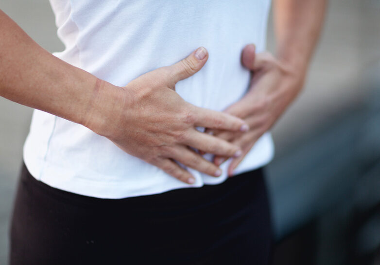 Close up of a woman holding the hands on abdomen, feeling her breath, outdoors during a yoga class