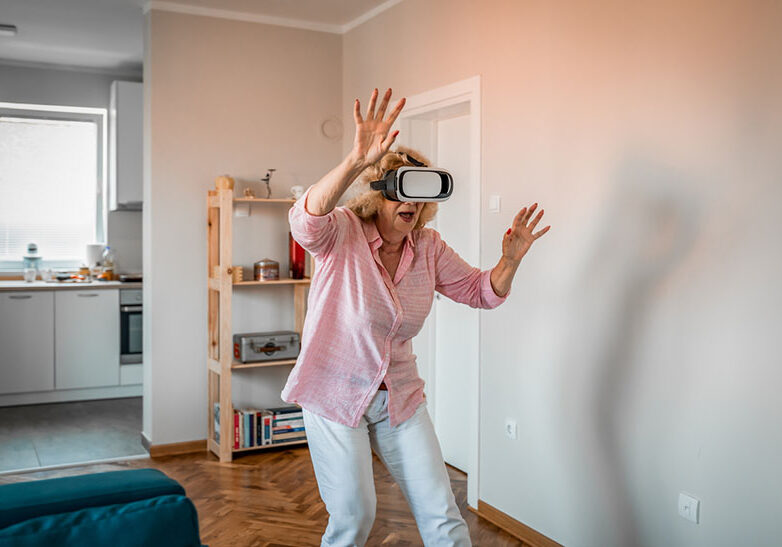 Happy senior woman having fun with vr headset.technology, augmented reality, gaming, entertainment and people concept - senior woman with virtual headset or 3d glasses playing videogame at home